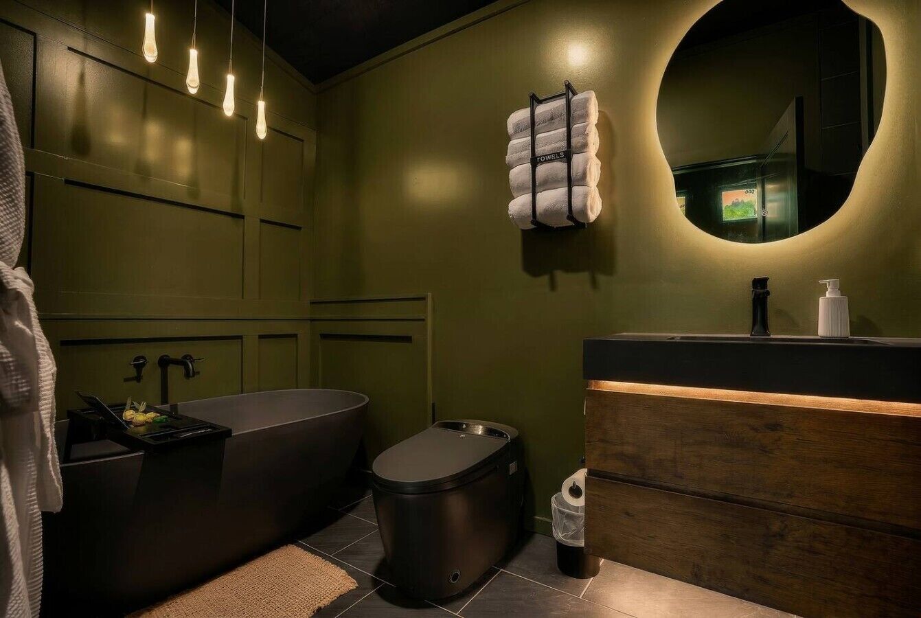 Een moderne badkamer met een groot ligbad, toilet, een wastafel met houten opbergmeubel en een handdoekrek met handdoeken.