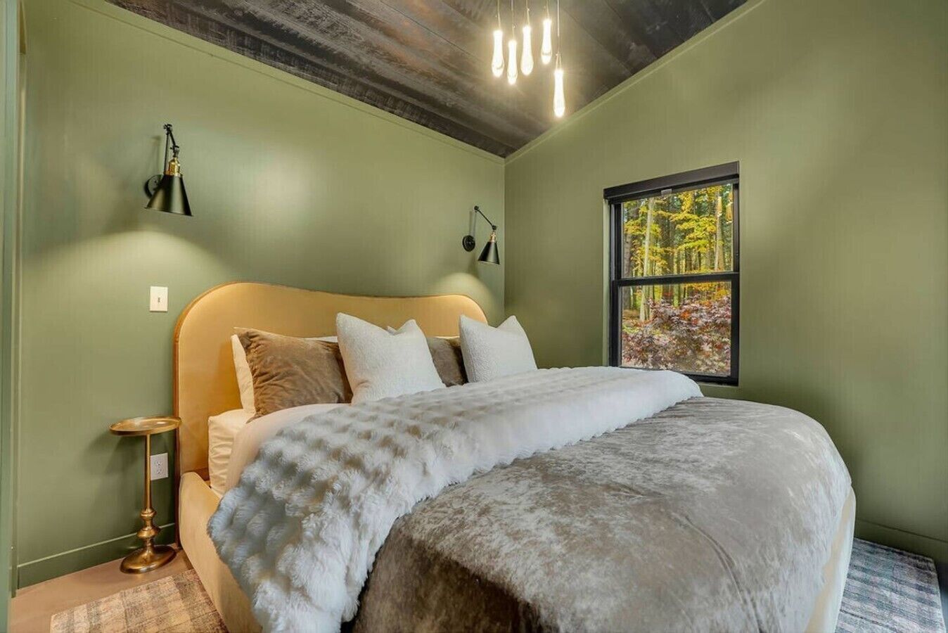 Une chambre à coucher avec un grand lit, une fenêtre donnant sur la forêt et un plafond avec des poutres apparentes.