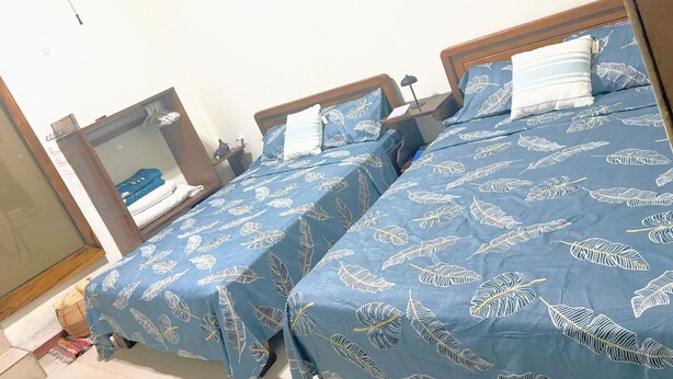 A bedroom with two beds, each with a blue bedspread featuring a leaf pattern. There is a wooden headboard, a bedside table with a lamp, and a mirror on the wall. - Cottage with a pool and natural surroundings—just 20 minutes from the beaches and Manuel Antonio Park! (Naranjito)