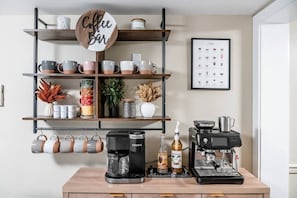 A coffee bar with a sign, shelves with mugs, a Keurig coffee maker, a Monin syrup bottle, and a coffee machine. - Riverfront Sauna! Sunken Hot Tub with river views! (Grantsville)