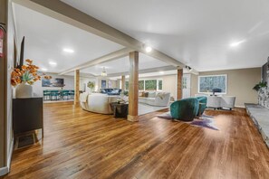 Un vaste espace de vie doté d’un plancher en bois, d’un canapé, d’un fauteuil turquoise et d’un coin repas avec des chaises.