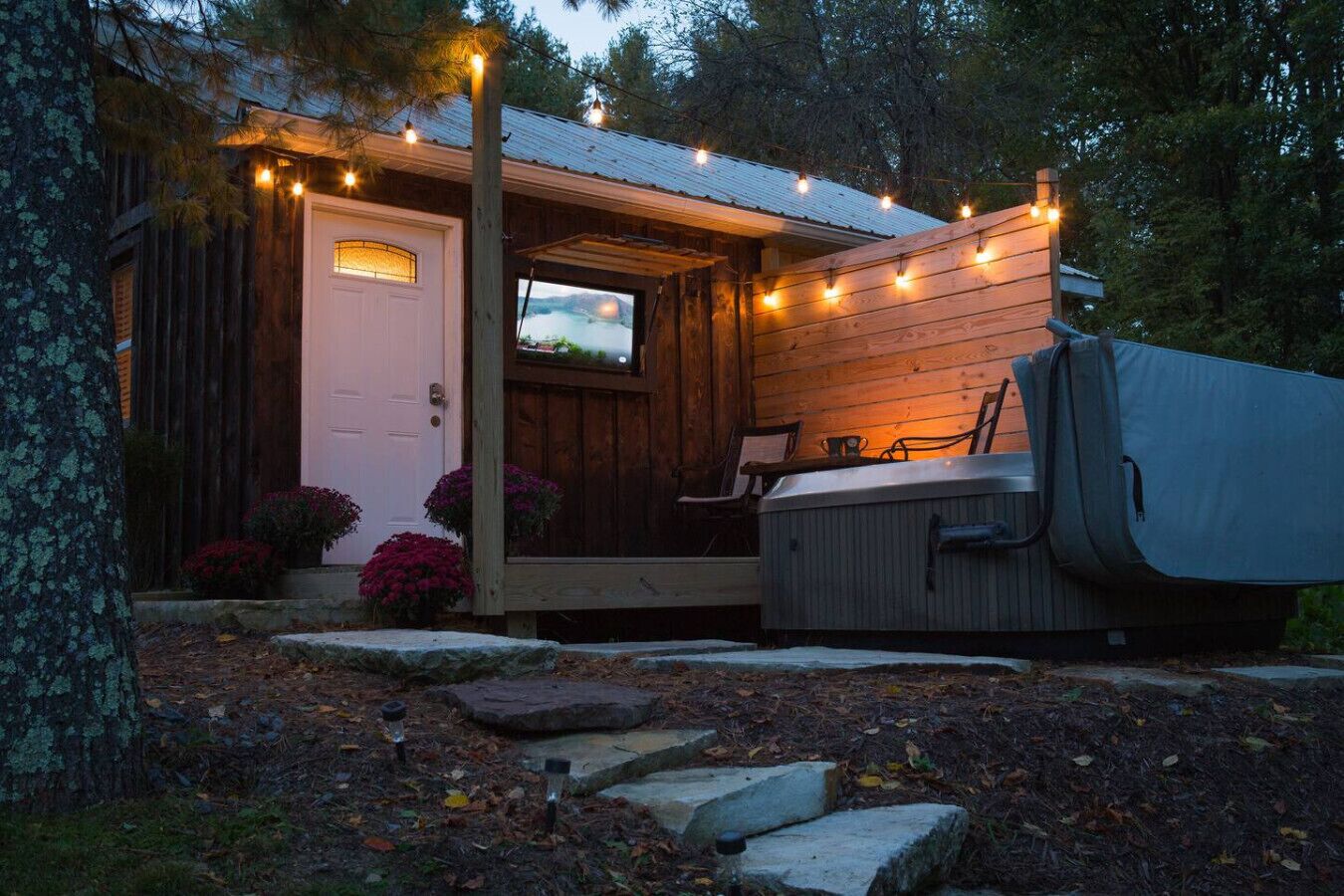 A cabin with a wooden exterior, a hot tub, and string lights.