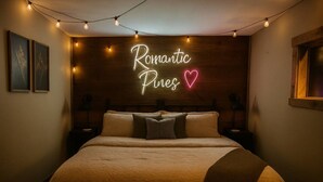 Une chambre avec un lit, un panneau lumineux au néon sur lequel on peut lire « Romantic Pines », et des guirlandes lumineuses.