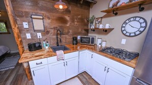 Une cuisine compacte avec des meubles blancs, un plan de travail en bois, un évier, un four à micro-ondes, une cuisinière et une horloge murale.