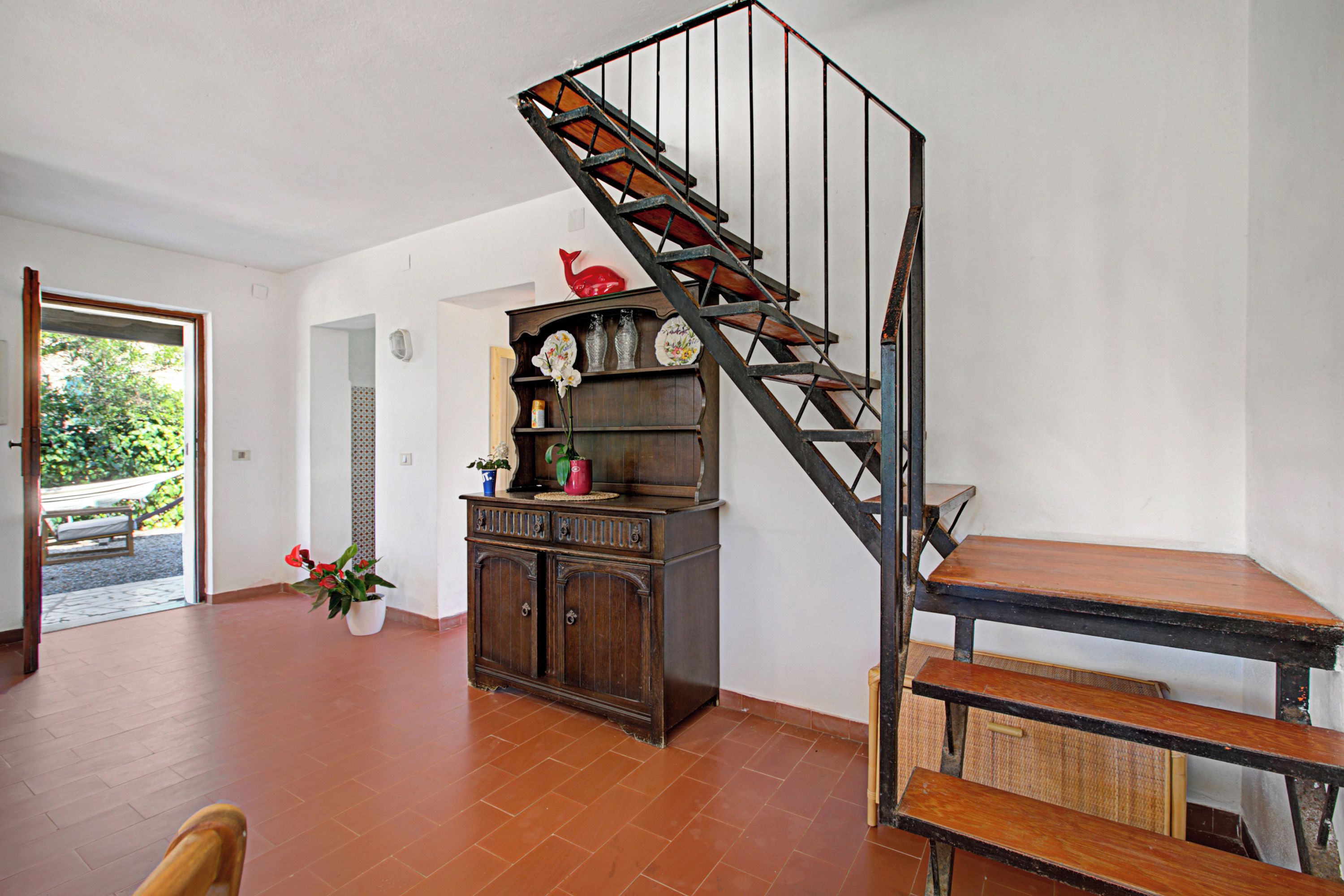 Una scala con finitura in legno e ringhiere in metallo, un armadio in legno con oggetti decorativi e una panca in una stanza con pavimento piastrellato.