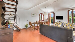 A spacious living area with a sofa, dining table, chairs, a staircase, and a TV.