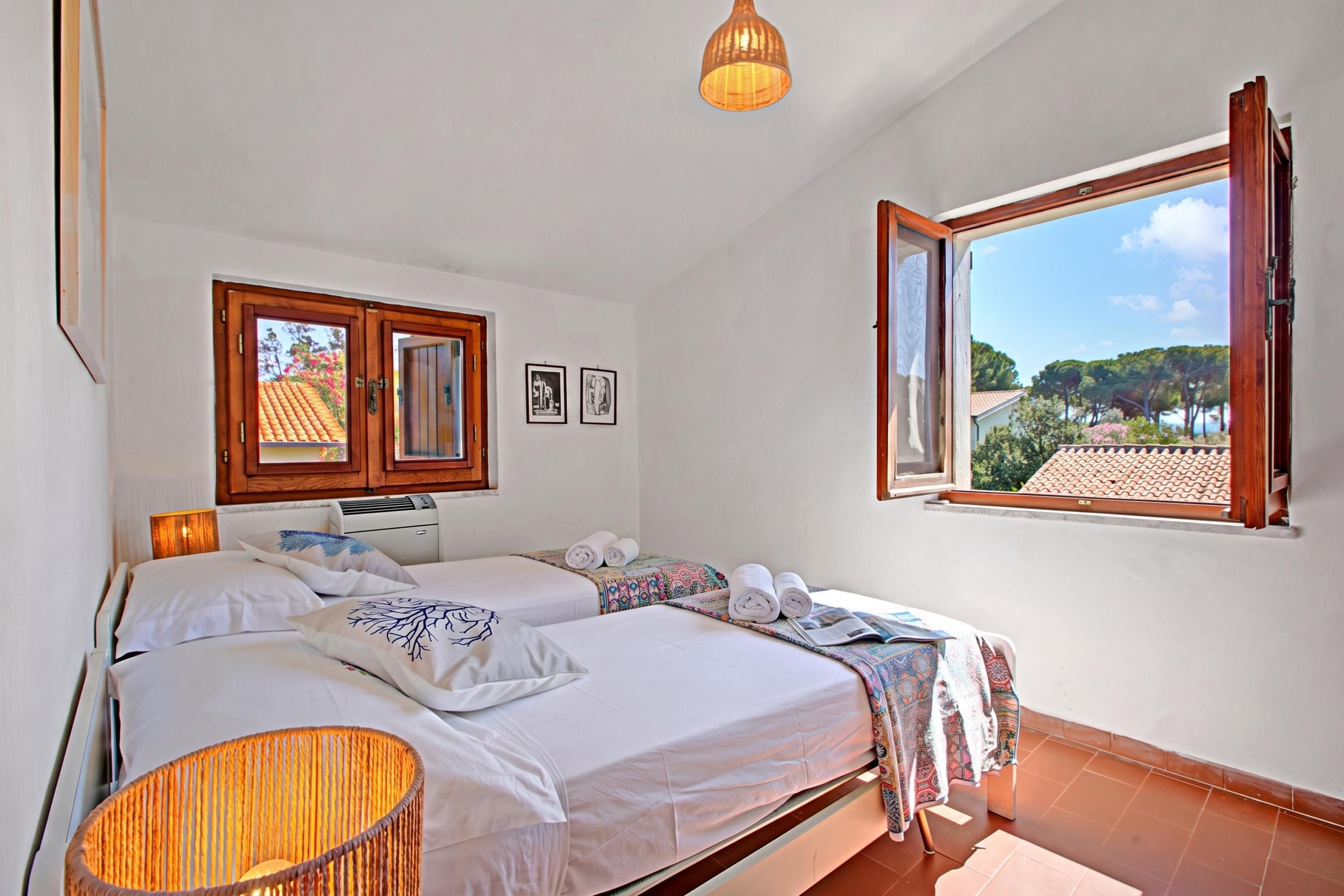 Quarto com duas camas, uma janela com a veneziana aberta e um candeeiro suspenso.