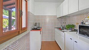 A compact kitchen with white cabinets, a red countertop, a stove, and a microwave.