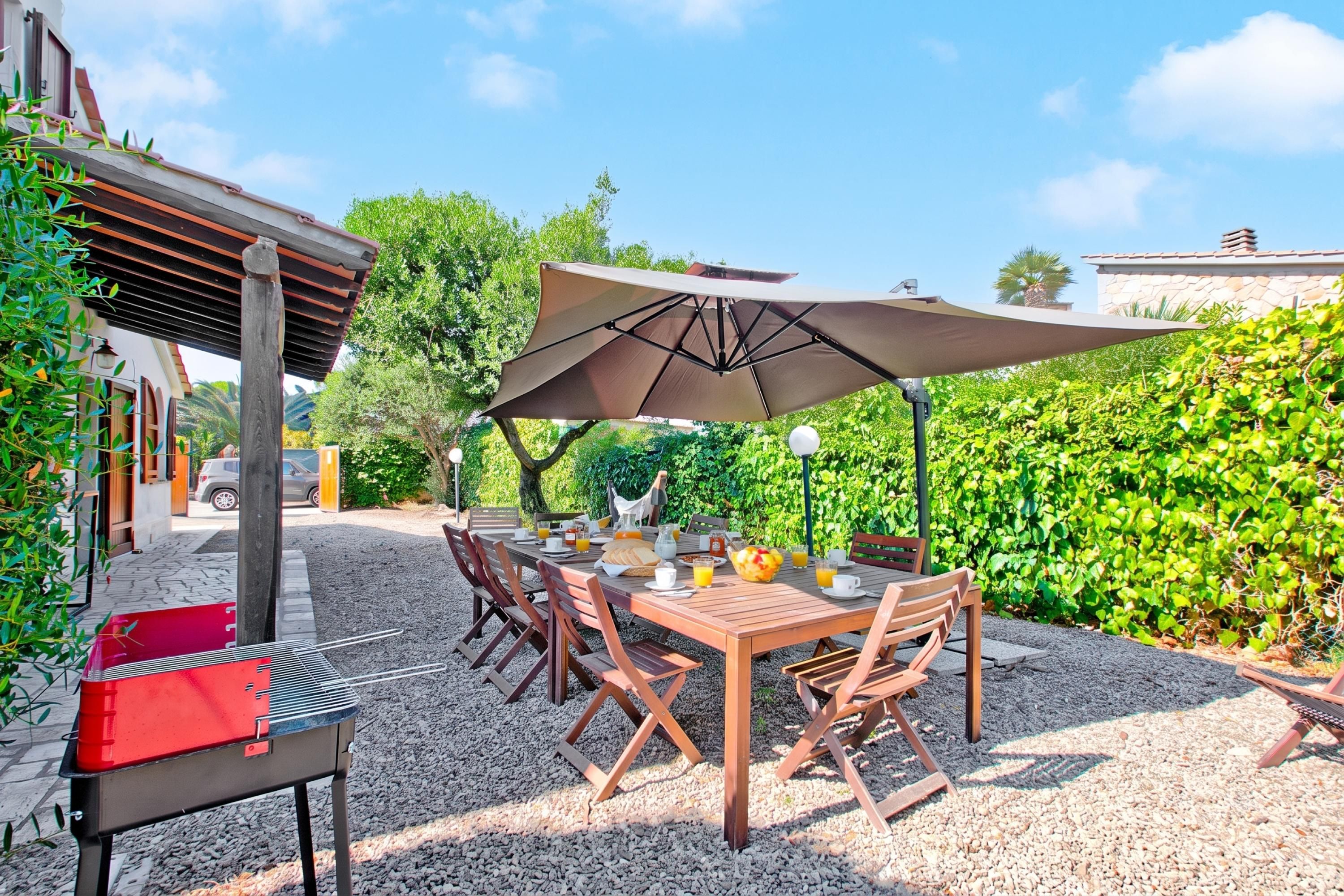 Un comedor al aire libre con una mesa dispuesta para cuatro personas, rodeada de sillas y protegida por un gran paraguas.