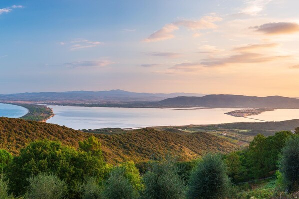 A coastal landscape with hills, a bay, and a distant mountain range.