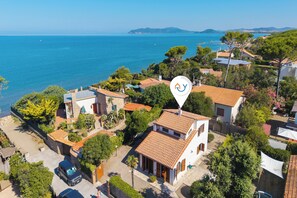 A coastal residential area with houses, a clear view of the sea, and a prominent navigation icon.