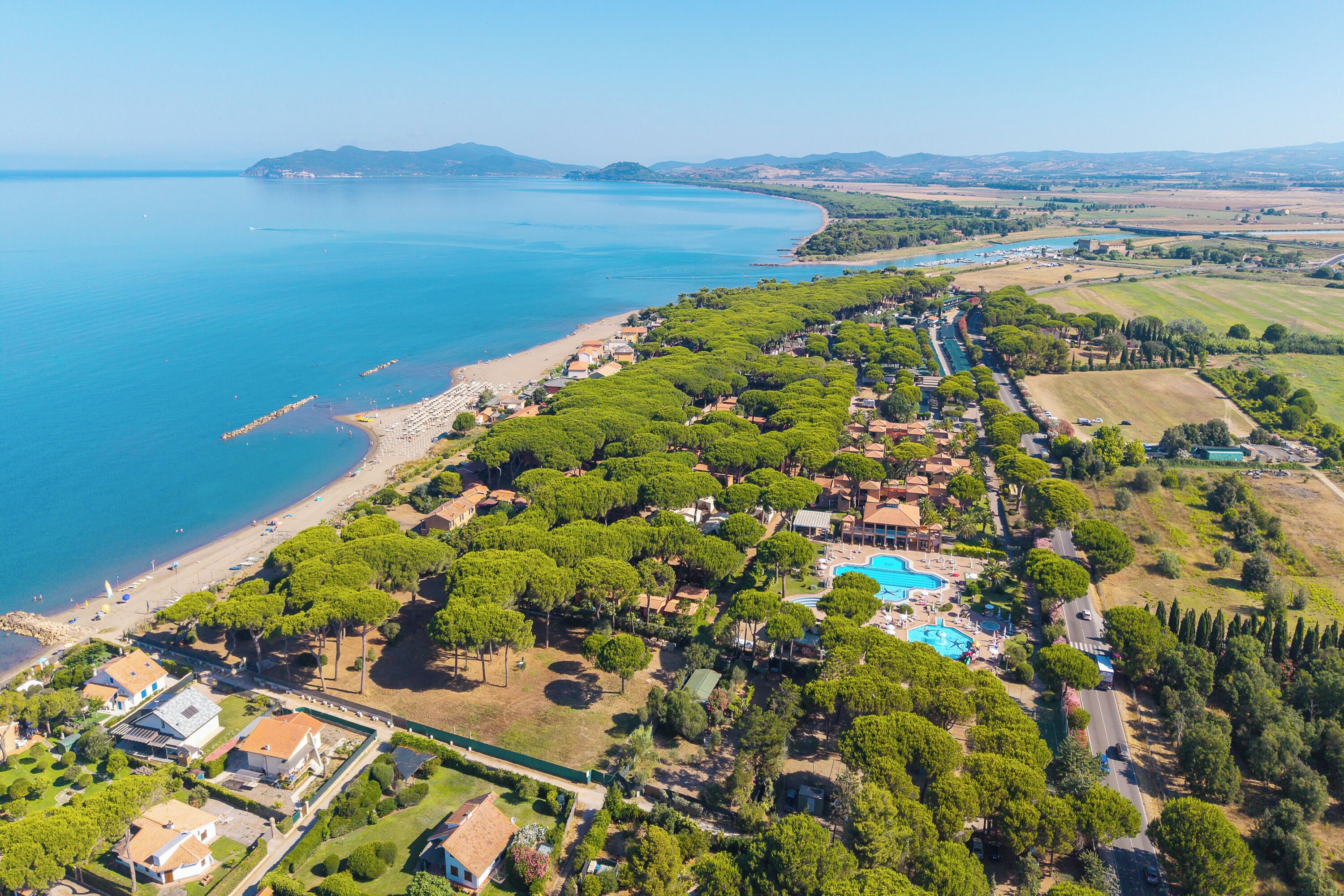 Luchtbeeld van een kustbezit met strand, zwembad en weelderige begroeiing.