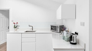 Ett modernt kök med vita köksskåp, en diskho i rostfritt stål, en mikrovågsugn och en vattenkokare på bänkskivan.
