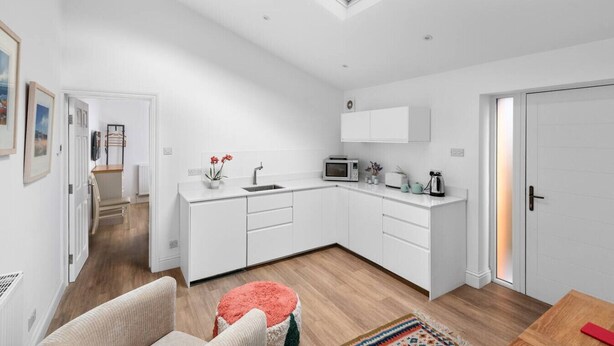 A modern kitchen with white cabinetry, a skylight, and a dining area with a table and chairs.