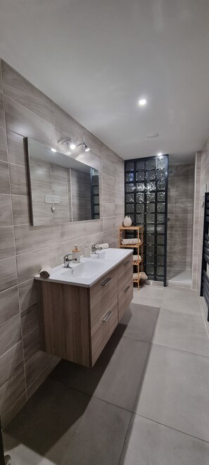 Een moderne badkamer met een grote spiegel, twee wasbakken, een houten wastafelmeubel en een glazen scheidingswand van zwart glas.