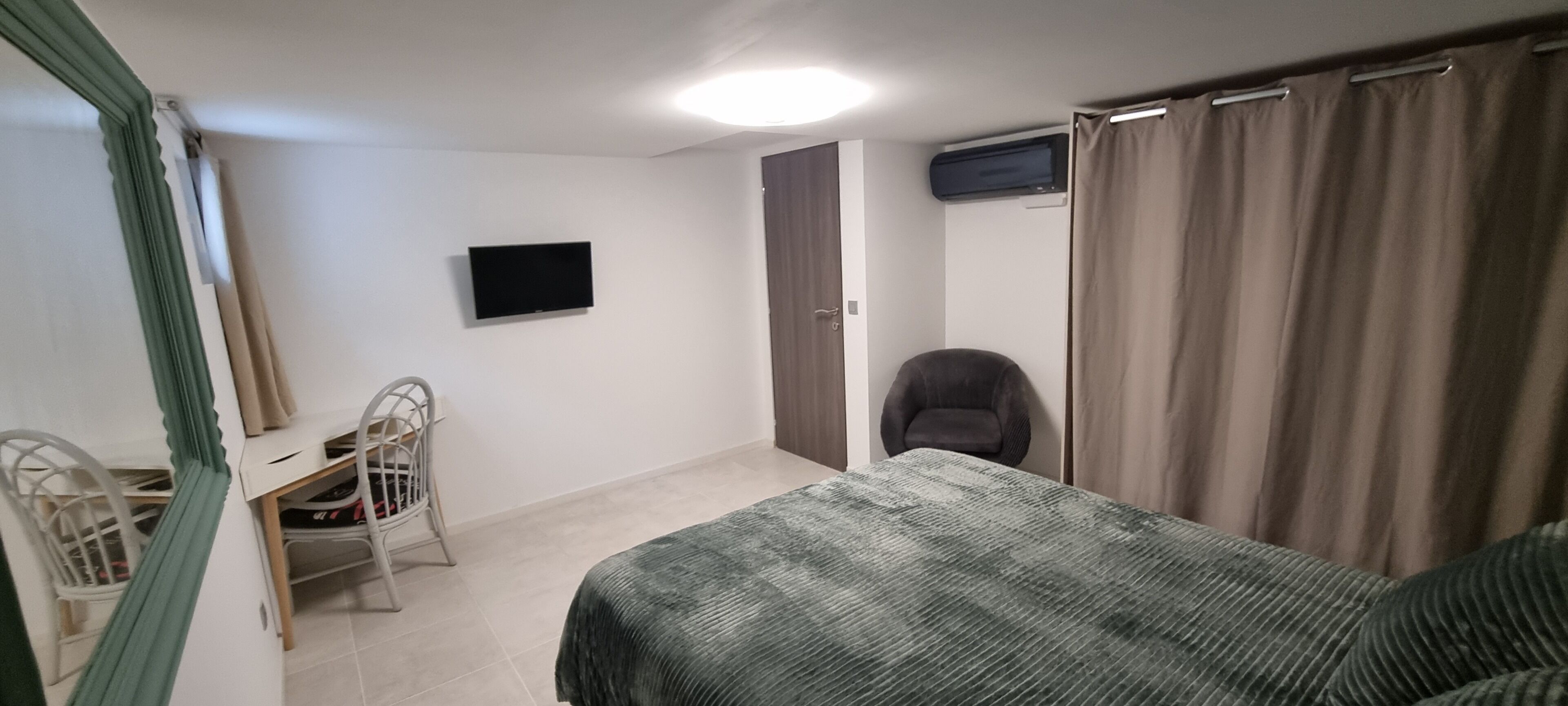 A bedroom with a bed, a chair, a desk, a television, and a door.