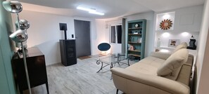 A modern living room with a sofa, a glass coffee table, a black cabinet, a floor lamp, and a bookshelf. - Ground-floor apartment in a villa complex with a pool (Le Broc)