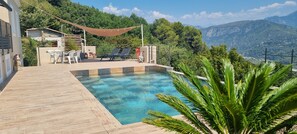 A pool area with a wooden deck, lounge chairs, and a view of mountains. - Ground-floor apartment in a villa complex with a pool (Le Broc)