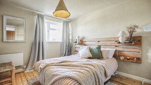Makuuhuone, jossa on puinen sängynpääty, raidallinen vuodevaatesetti, riippuvalaisin, peili ja ikkuna, jossa on verhot.