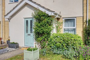 Et hus med en lyseblå dør, en lille have med forskellige planter, og en hvid facade.