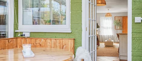 Une pièce avec une table en bois, une chaise blanche, une grande fenêtre et un mur vert.