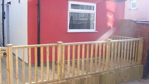 A wooden deck with a railing, a red wall, and a window. - Funky Easton flat with parking (Greenbank)