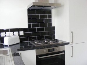 A kitchen with a gas stove, a toaster, and white cabinets. - Funky Easton flat with parking (Greenbank)