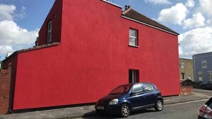A red building with a single window and a car parked in front. - Funky Easton flat with parking (Greenbank)