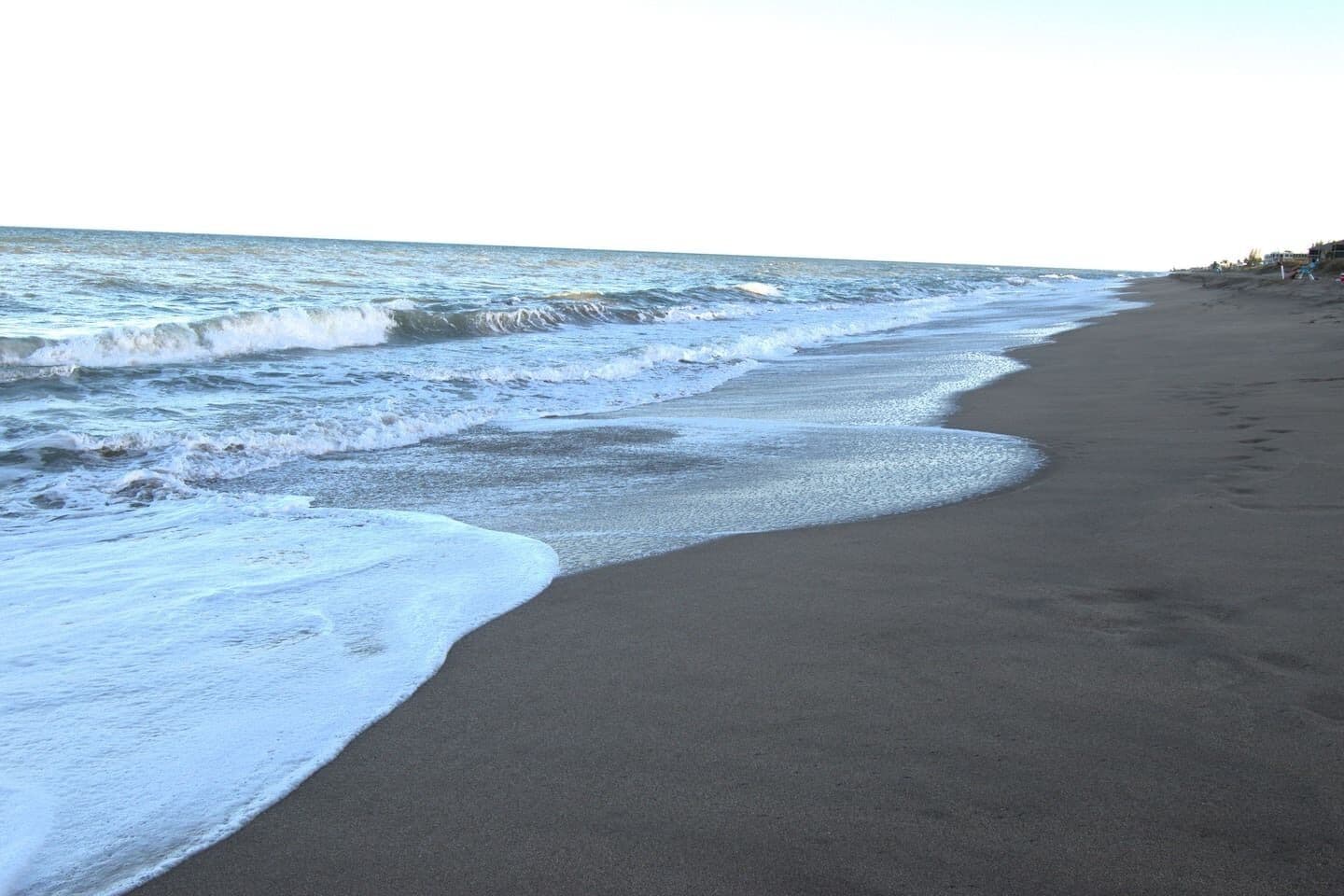 Una playa con olas, una orilla arenosa y cielo despejado.