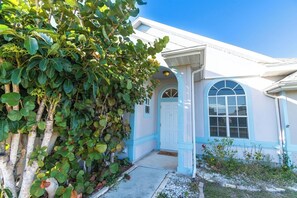 A house with a white exterior and blue trim, a front door, and a large window. - Fun Hot Tub & Pool Beach Home - Pet Friendly (Port St. Lucie)