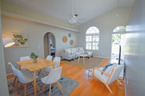 Un vaste espace de vie comprenant une table à manger, des chaises blanches, un canapé et un téléviseur.