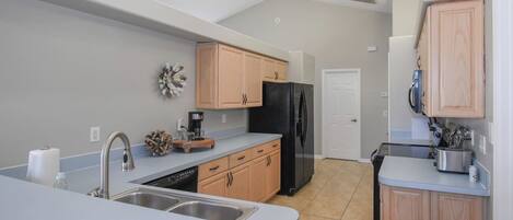 A modern kitchen with light wood cabinets, a black refrigerator, and a dishwasher.