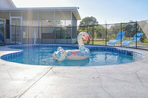 A swimming pool with a swan inflatable, a covered patio, and a fenced area with lounge chairs. - Fun Hot Tub & Pool Beach Home - Pet Friendly (Port St. Lucie)