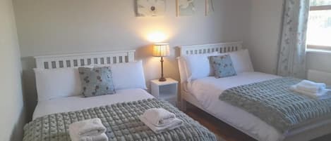 A bedroom with two beds, a bedside table with a lamp, and a window with curtains.