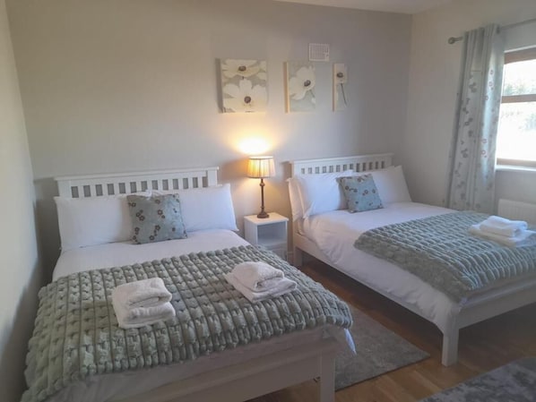 Un dormitorio con dos camas, una mesita de noche con lámpara y una ventana con cortinas.