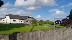 A two-story building with a stone facade and a grey roof, surrounded by a well-maintained lawn and a stone wall. - St John s B and B (Lecarrow)