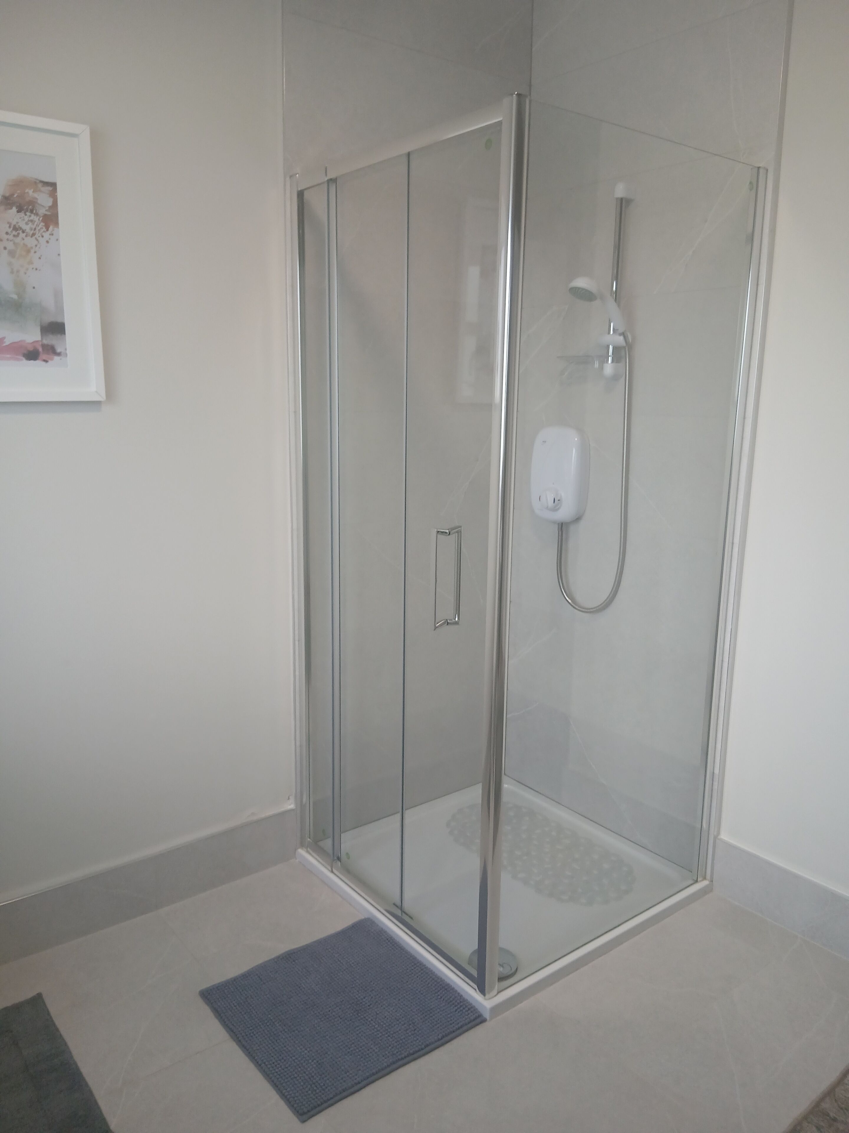 A glass-enclosed shower with a handheld showerhead and a control panel.