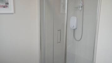 A glass-enclosed shower with a handheld showerhead and a control panel.