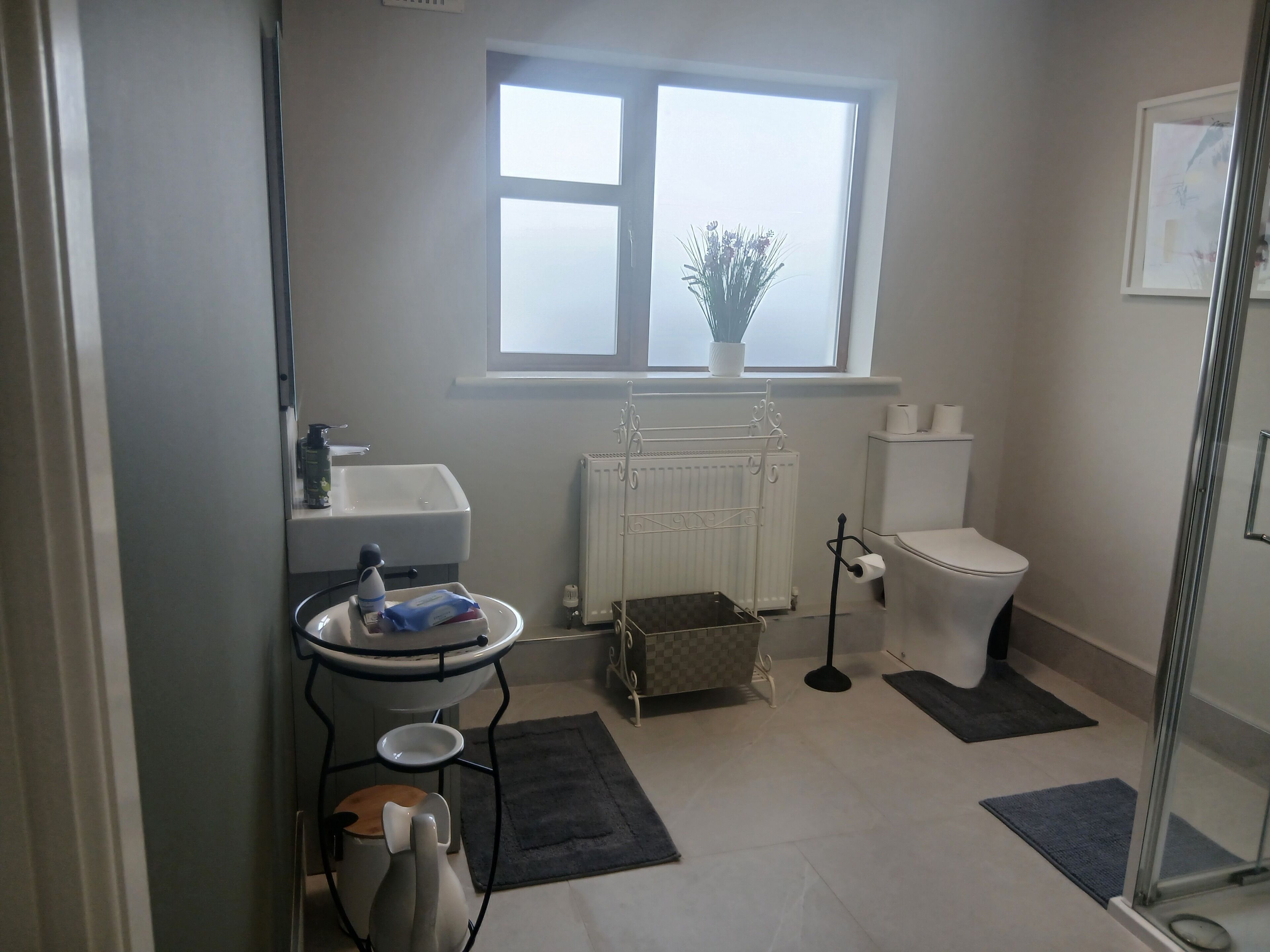 A bathroom with a toilet, sink, radiator, and a window with a plant.