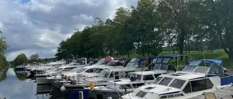 A marina with boats docked along a calm waterway, surrounded by trees and a clear sky.