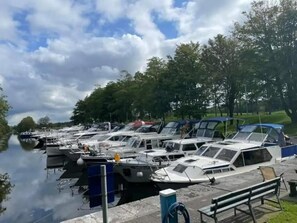 Een jachthaven met boten afgemeerd langs een rustig water, omgeven door bomen en een heldere lucht.