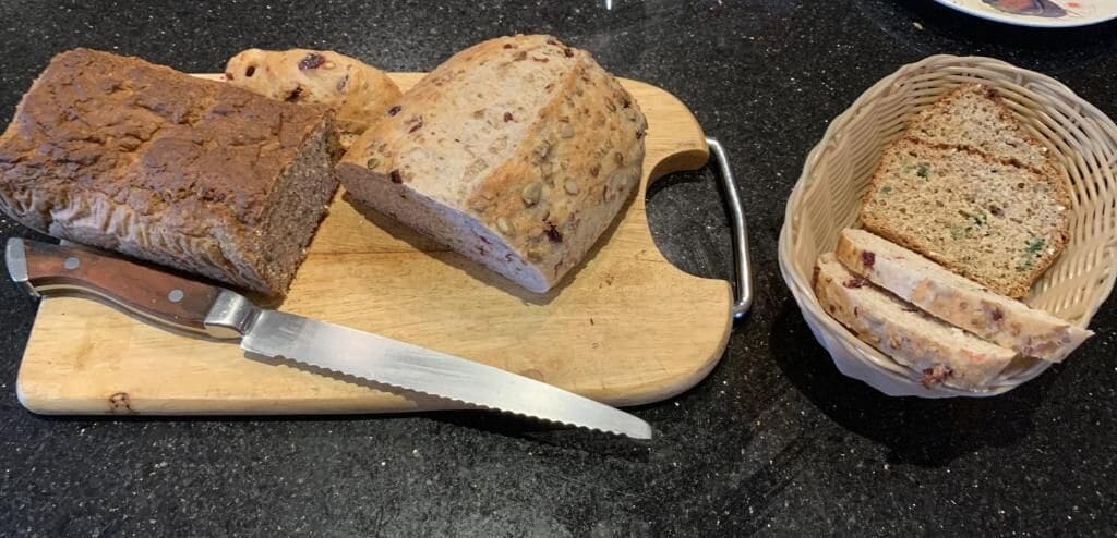A loaf of bread on a cutting board with a knife, and a basket with sliced bread.