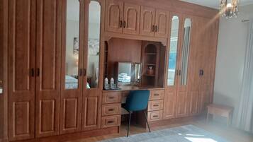 A room with a large wooden wardrobe, a desk with a chair, a mirror, and a hanging light fixture.
