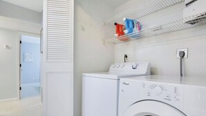 A laundry room with a washer and dryer, a shelf with detergent bottles, and a door leading to another room. - 3/2 Heated Pool • Close to Beach • Trails • Golf (Port St. Lucie)