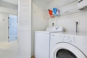A laundry room with a washer and dryer, a shelf with detergent bottles, and a door leading to another room. - 3/2 Heated Pool • Close to Beach • Trails • Golf (Port St. Lucie)