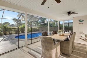 An outdoor patio with a dining table, chairs, and a view of a swimming pool.
