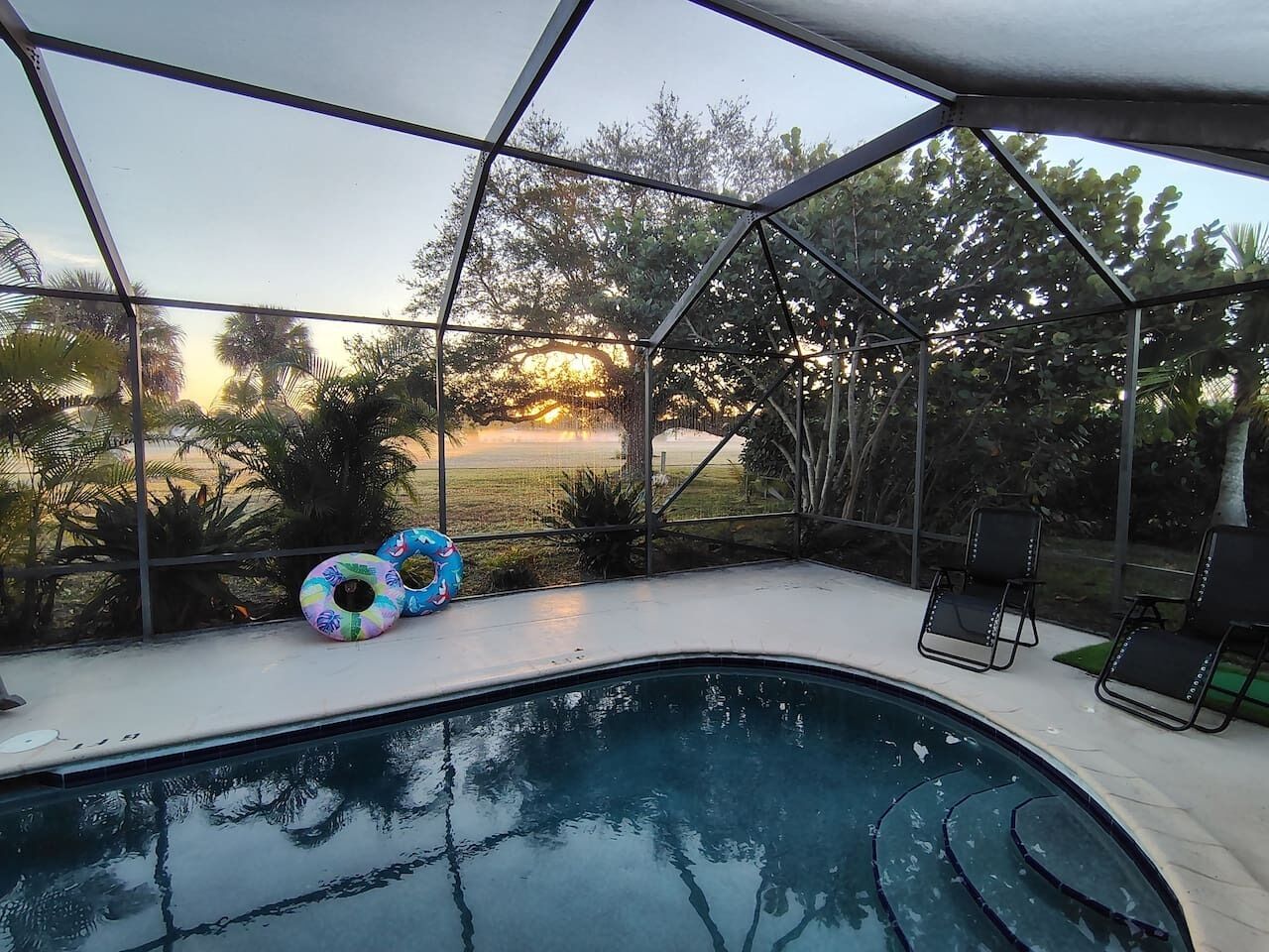A swimming pool with a glass enclosure, surrounded by lounge chairs and inflatable rings.