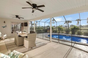 A room with a pool, wicker furniture, ceiling fans, and large windows.