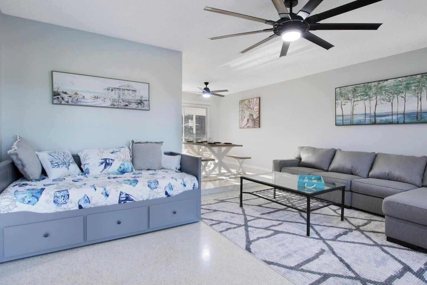 A modern living room with a grey sofa, a blue sofa with a patterned cover, a coffee table, and a ceiling fan.