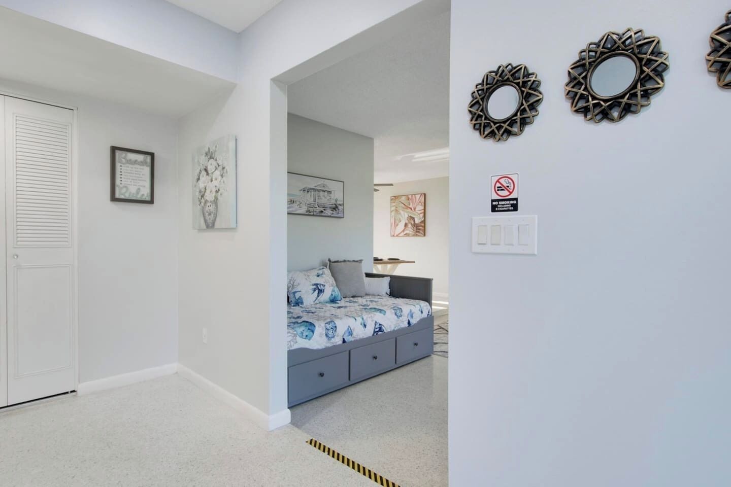 Quarto com cama, mesa de cabeceira, espelho fixado na parede e porta com veneziana.